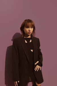 a woman in a black suit posing against a purple wall