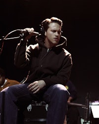 a man in a black hoodie sitting on a stool
