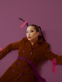 a woman in a brown trench coat laying on a purple wall